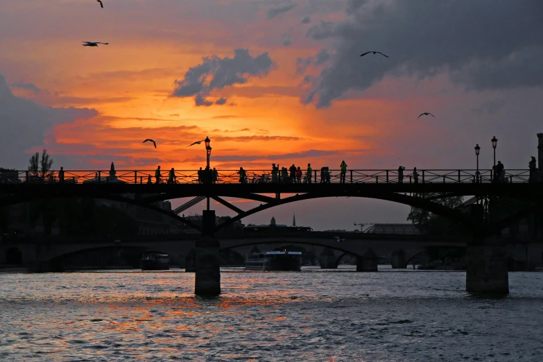 a group of people walking across a bridge over a river, pexels contest winner, romanticism, orange and red sky, paris, annie liebowitz, slide show