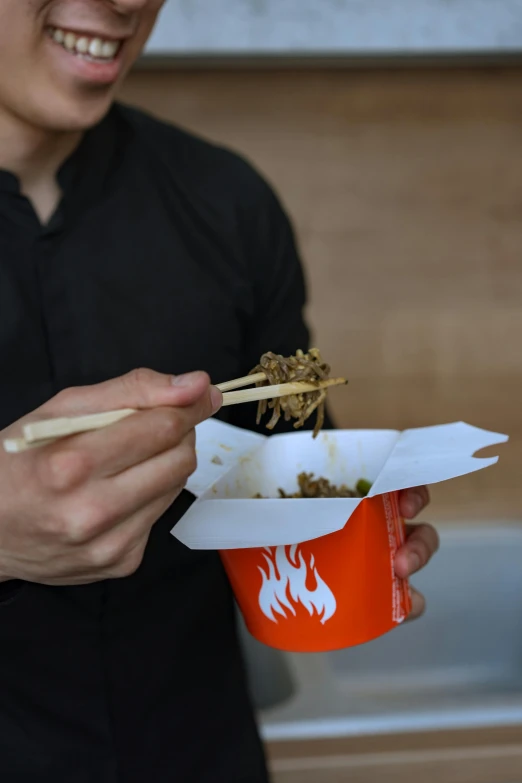 a man holding a bowl of noodles and chopsticks, by Adam Pijnacker, burning wings, cardboard, close - up photo, exterior shot