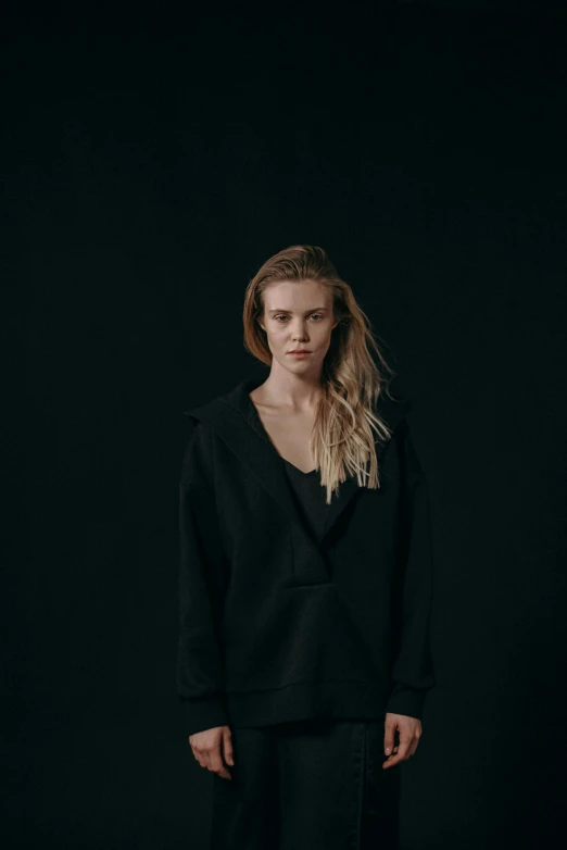 a woman standing in front of a black background, inspired by Louisa Matthíasdóttir, unsplash, antipodeans, samara weaving, rugged black clothes, looking confused, asher duran