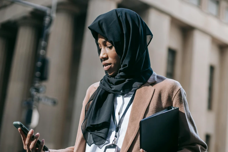 a woman in a hijab is looking at her cell phone, trending on pexels, hurufiyya, wearing robes and neckties, royal commission, walking down, panel of black