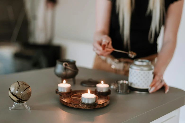 a woman lighting candles on top of a counter, a still life, trending on pexels, moroccan tea set, grey, acupuncture treatment, blurred