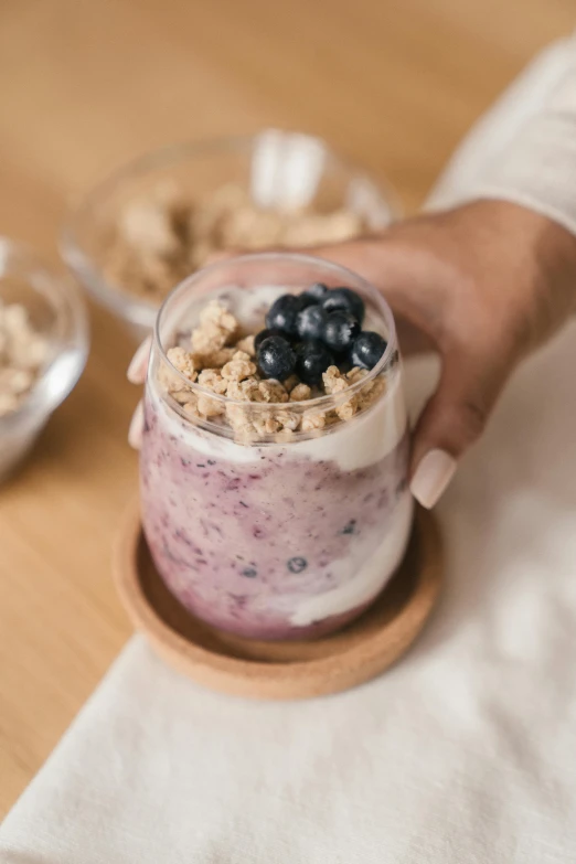 a close up of a person holding a cup of food, blueberry, with clear glass, product shot, yogurt