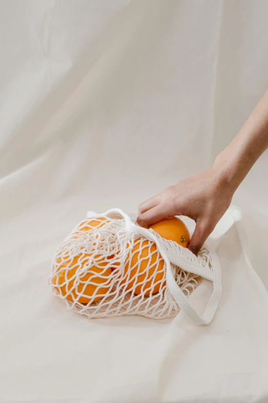 a person holding an orange in a mesh bag, unsplash, net art, white loincloth, getting groceries, strings, cream