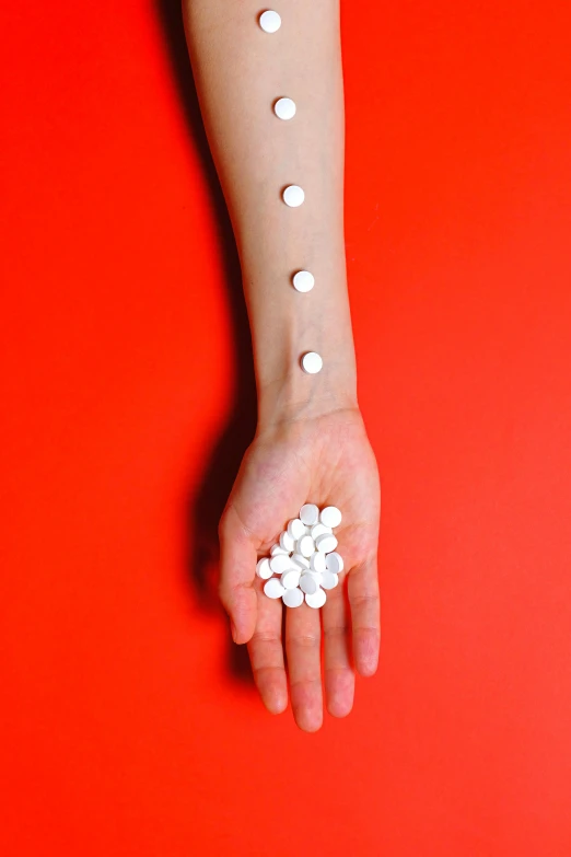 a person holding a bunch of pills in their hand, a tattoo, by Gavin Hamilton, antipodeans, white pearlescent, made of nanomaterials, ( ( photograph ) ), red and white