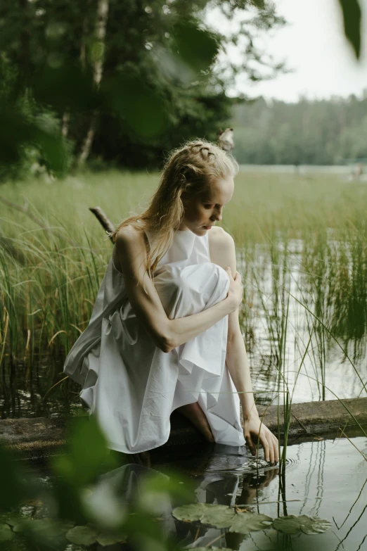 a woman sitting on a log in the water, by Grytė Pintukaitė, pexels contest winner, renaissance, nico wearing a white dress, finland, embracing, young blonde woman