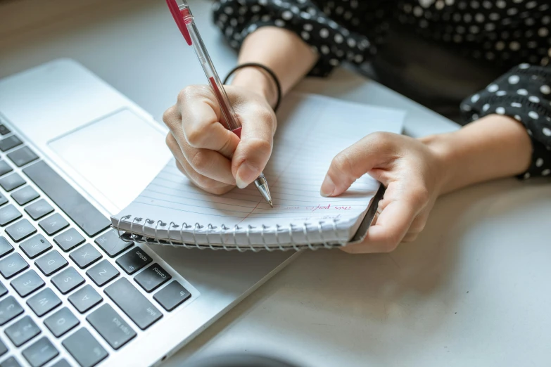 a woman writing in a notebook next to a laptop, by Nicolette Macnamara, trending on pexels, academic art, bottom angle, wikihow, holding a clipboard, student