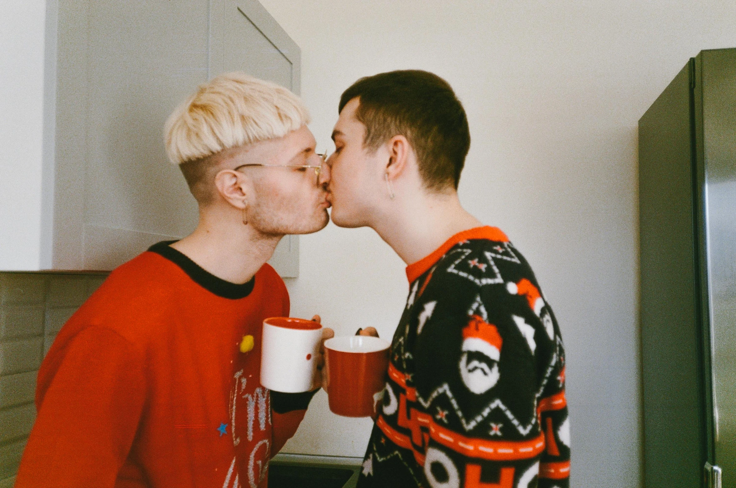 a couple of men standing next to each other in a kitchen, by Attila Meszlenyi, pexels, both have red lips, with a cup of hot chocolate, albino hair, lesbian kiss