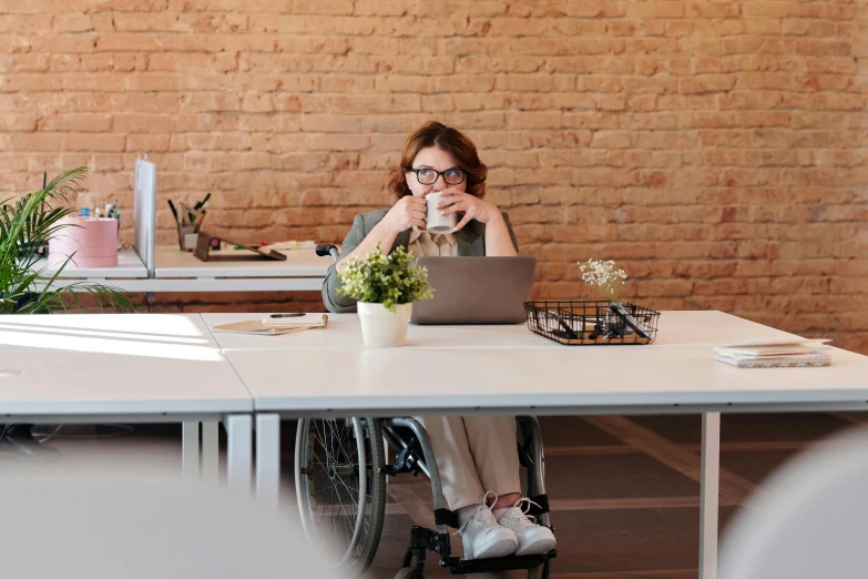 a woman sitting at a table with a laptop, wheelchair, wētā fx, busy people, covid