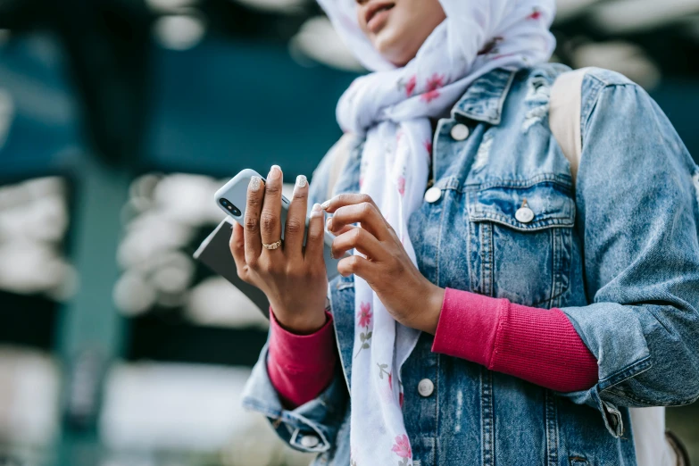 a woman in a hijab using a cell phone, trending on pexels, jean jacket, pink white turquoise, with index finger, handheld