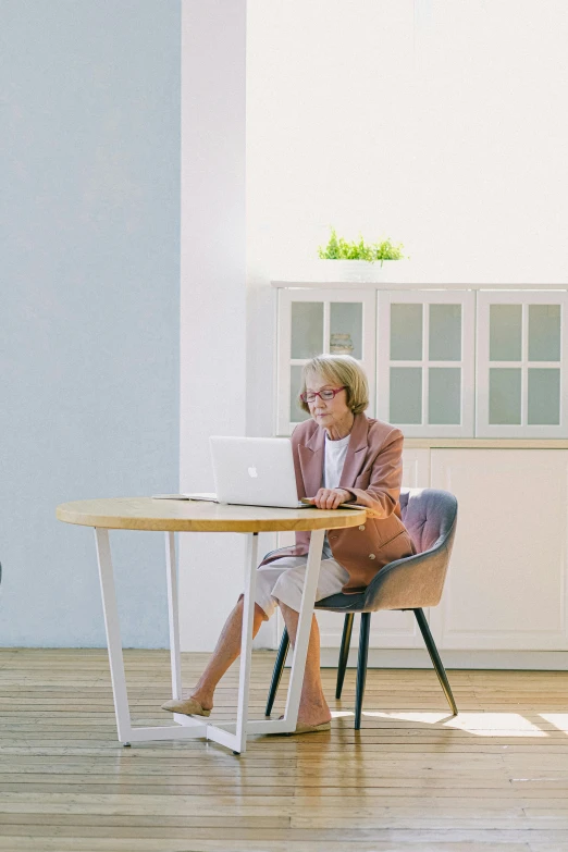 a woman sitting at a table using a laptop computer, by Jang Seung-eop, trending on unsplash, renaissance, fullbody photo, minimalist furniture, youtube video screenshot, older woman