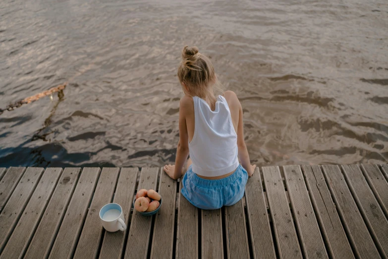 a woman sitting on a dock next to a body of water, by Maud Naftel, pexels contest winner, breakfast, physical : tinyest midriff ever, young girl, blue