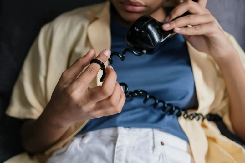 a woman sitting on a couch talking on a phone, trending on pexels, hyperrealism, wearing two metallic rings, black wired cables, tailored clothing, black jewellery