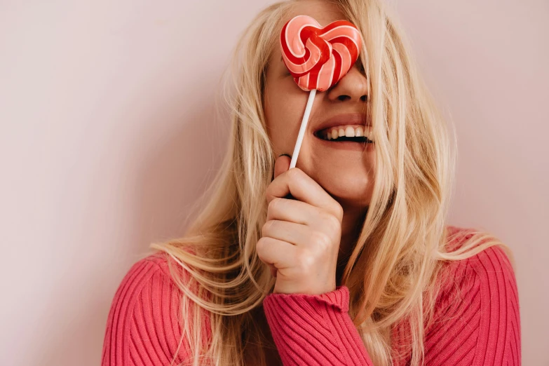 a woman holding a lollipop in front of her face, trending on pexels, head bent back in laughter, ((pink)), blond, candy decorations