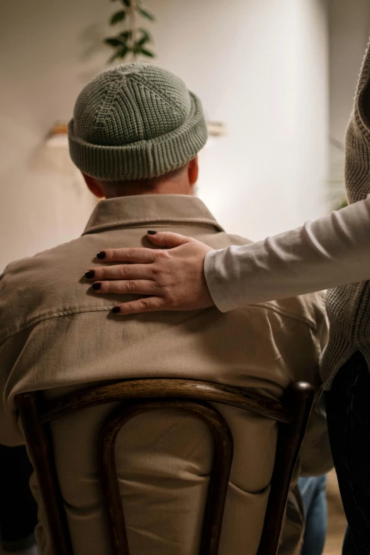 a man sitting on top of a chair next to a woman, by Jesper Knudsen, trending on pexels, renaissance, nursing home, two men hugging, brown clothes, hand holding cap brim