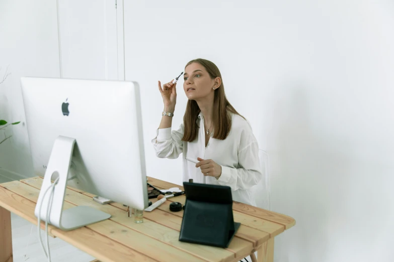 a woman sitting at a desk in front of a computer, a hyperrealistic painting, trending on pexels, putting makeup on, female in office dress, in white room, minimalissimo