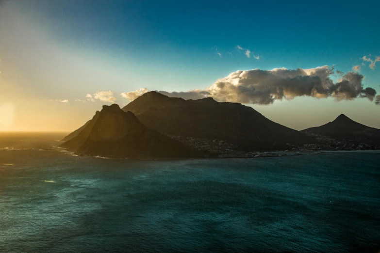 a large body of water with a mountain in the background, by Daniel Lieske, unsplash contest winner, cape, late afternoon sun, extreme panoramic, over the ocean