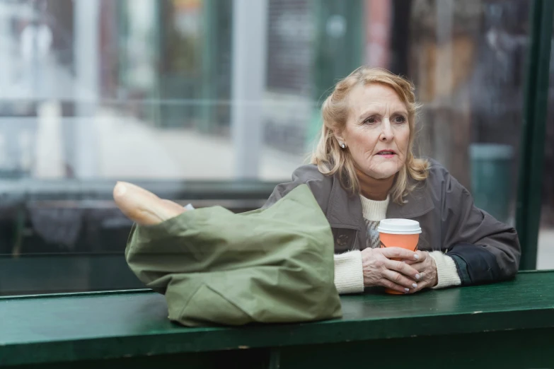 a woman sitting on a bench holding a cup of coffee, by David Begbie, gillian anderson, skilled homeless, promo image, flattened