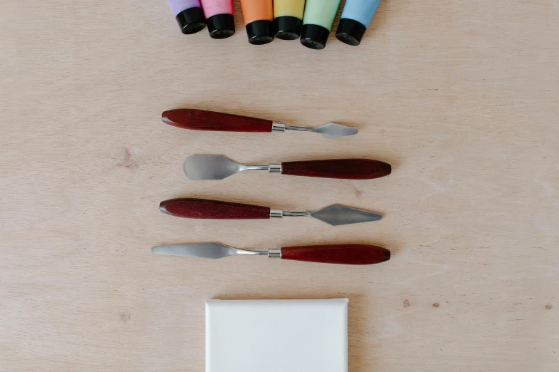 a group of knives sitting on top of a wooden table, a still life, inspired by Kyffin Williams, process art, spatula, multicoloured, miniature product photo, white