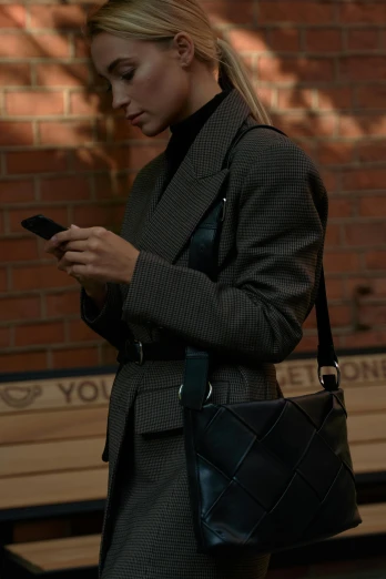 a woman is looking at her cell phone, by Nina Hamnett, happening, leather straps, tailored clothing, square, bag
