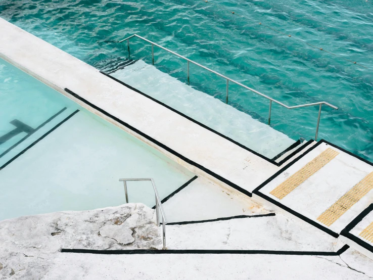 a man riding a skateboard up the side of a ramp next to a swimming pool, an album cover, by Carey Morris, unsplash contest winner, modernism, stone steps, on the ocean water, sydney hanson, white travertine terraces