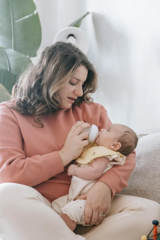 a woman sitting on a couch feeding a baby, pexels contest winner, renaissance, holding a bottle, beige, organic, soft - warm