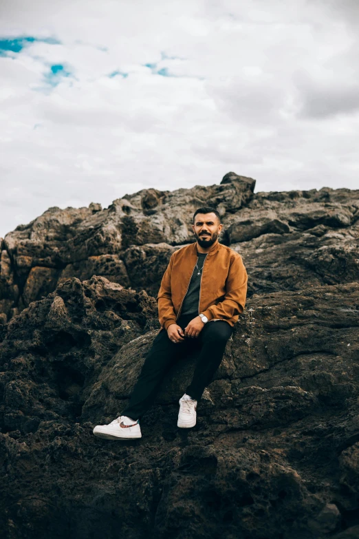 a man sitting on a rock on a cloudy day, an album cover, pexels contest winner, lyco art, a portrait of rahul kohli, in australia, сastle on the rock, sneaker photo