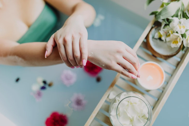 a woman sitting in a bath tub holding a jar of cream, trending on pexels, graceful arms, hand on table, manuka, extremely graphic