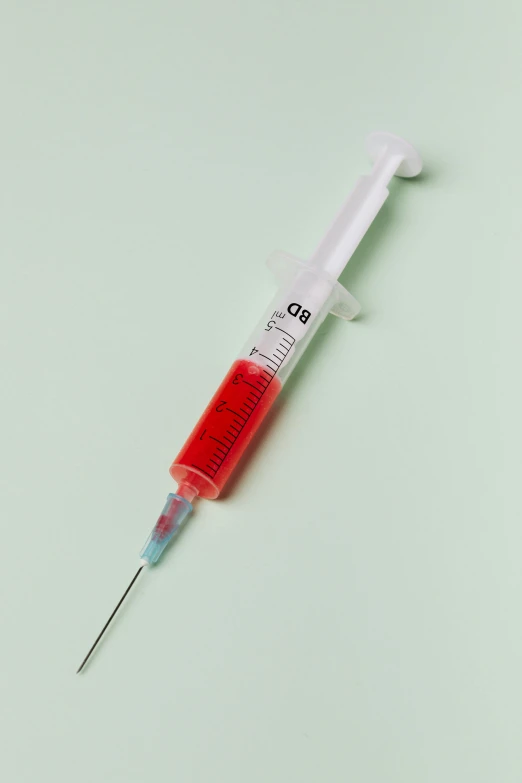 a syet sitting on top of a green surface, by Bryan Organ, unsplash, holding syringe, red color bleed, on a pale background, highly detailed product photo