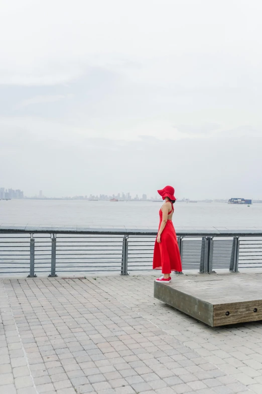 a woman in a red dress and a red hat, inspired by Fei Danxu, harbour in background, boardwalk, wide - shot, skyline