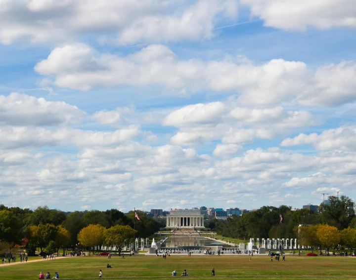 a group of people standing on top of a lush green field, by Kristin Nelson, pexels contest winner, neoclassicism, destroyed washington dc, capital plaza, clouds around, during autumn