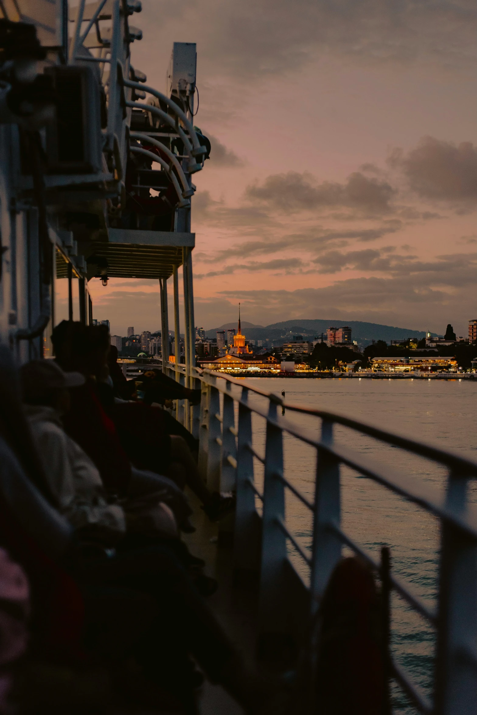 a group of people sitting on top of a boat, vista of a city at sunset, on the deck of a ship, split near the left, low light cinematic