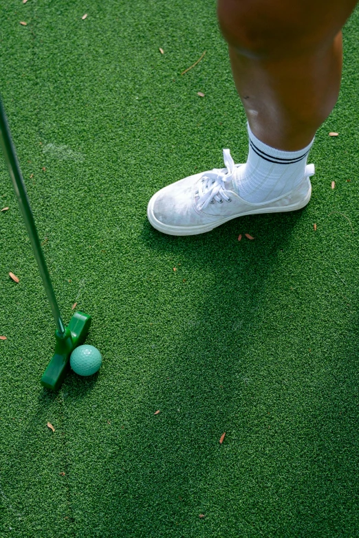 a man standing on top of a green field next to a golf ball, green floor, neck zoomed in, off putting, sports setting