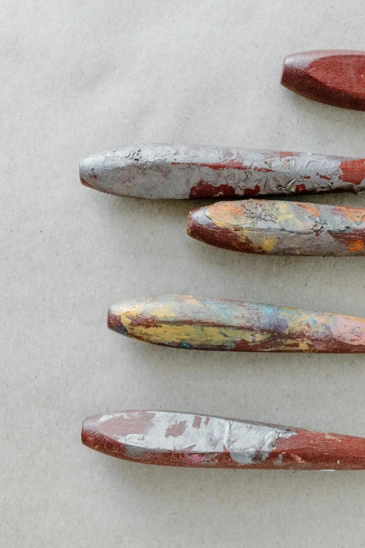 a group of knives sitting on top of a table, metallic flecked paint, burnt sienna and venetian red, rainbow coloured rockets, slate