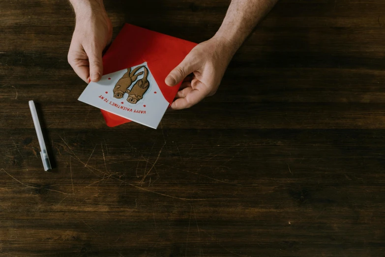 a person holding a card on top of a wooden table, by Julia Pishtar, pexels contest winner, red shoes, holiday, diecut, maintenance photo