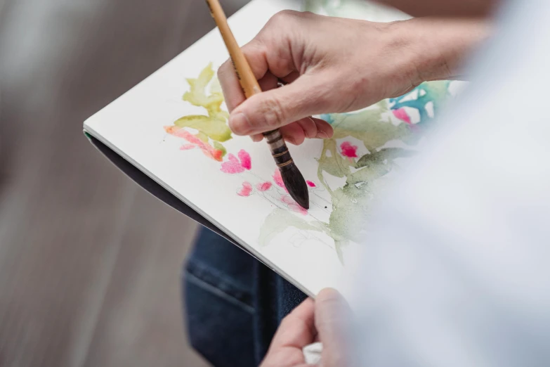 a close up of a person painting with a brush, a watercolor painting, trending on pexels, fan favorite, botanic watercolors, holding pencil, mixed art