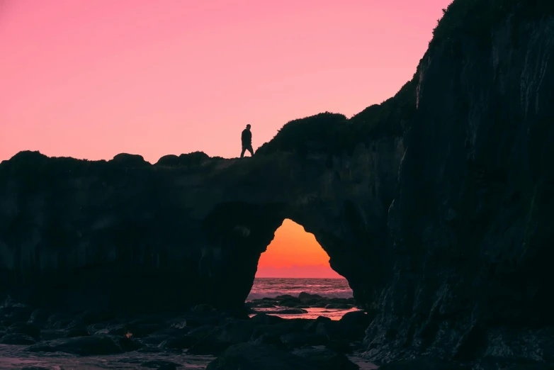 a person standing on top of a rock formation, by Jessie Algie, pexels contest winner, romanticism, pink arches, human silhouette, california coast, an archway
