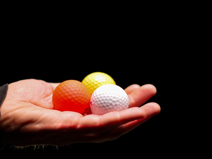 a person holding three golf balls in their hand, by Jan Rustem, unsplash, colored gels, practice, on black background, an orange