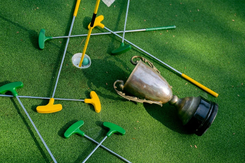 a metal trophy sitting on top of a green field, inspired by Shirley Teed, clubs, scattered props, green and yellow, on ground