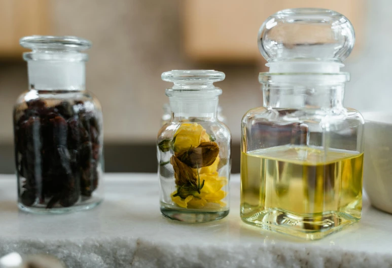 a close up of three bottles of oil on a counter, a still life, unsplash, renaissance, botanical herbarium, petals, beakers, synthetic materials