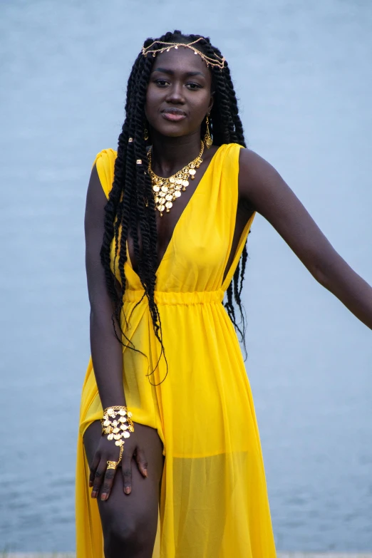 a woman in a yellow dress standing next to a body of water, inspired by Ras Akyem, pexels, afrofuturism, gold chains, black teenage girl, black jewelry, adut akech