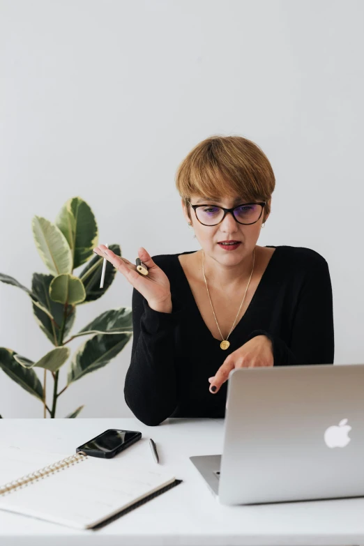 a woman sitting at a desk in front of a laptop, trending on pexels, renaissance, giving a speech, wearing black rimmed glasses, scolding, next to a plant