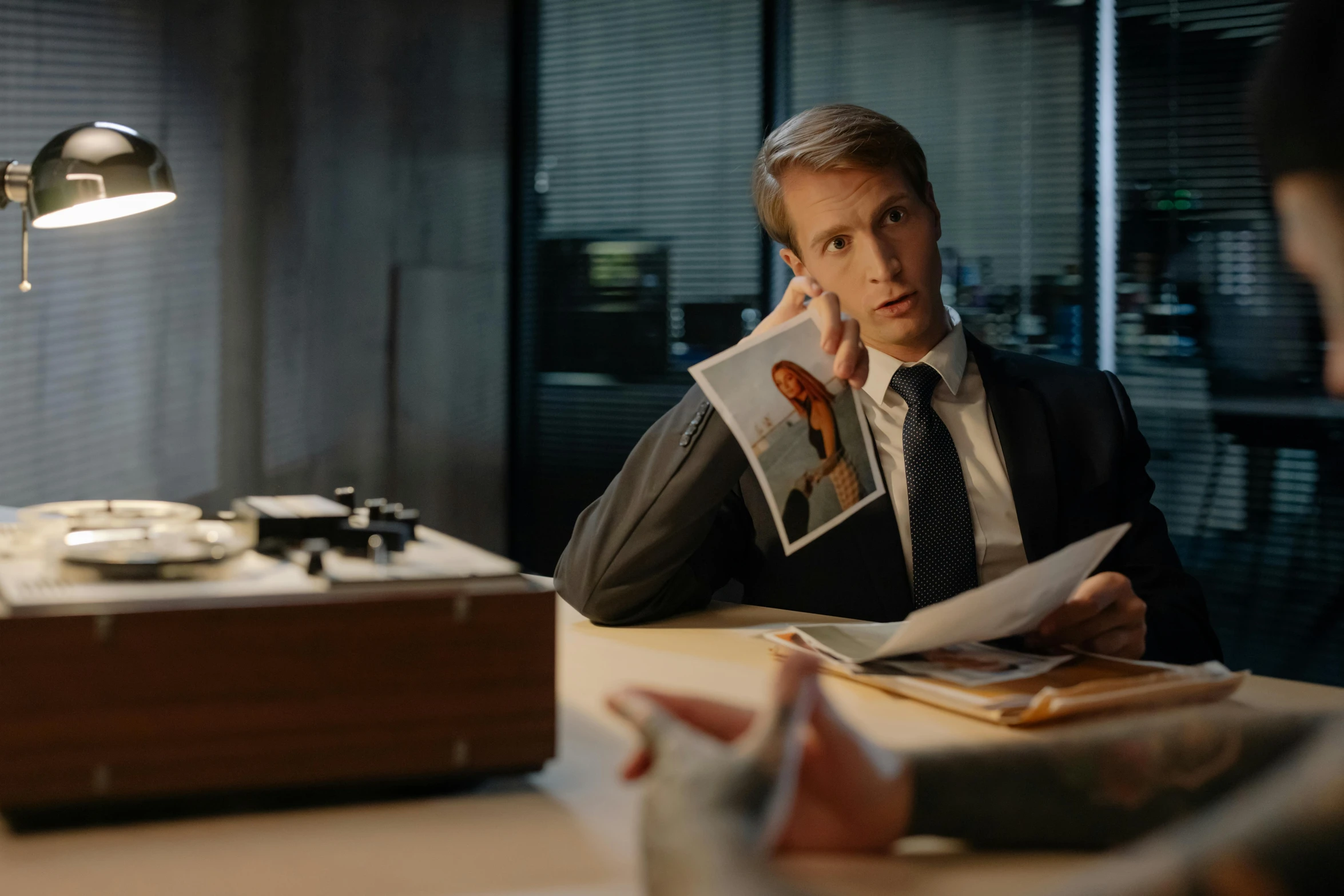 a man sitting at a desk talking on a cell phone, unsplash, photorealism, still image from tv series, caspar david, looking for clues, in his suit