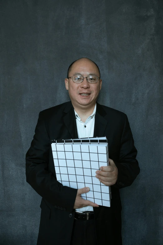 a man in a suit holding a piece of paper, an album cover, inspired by Fei Danxu, standing with a black background, holding notebook, architect, no - text no - logo