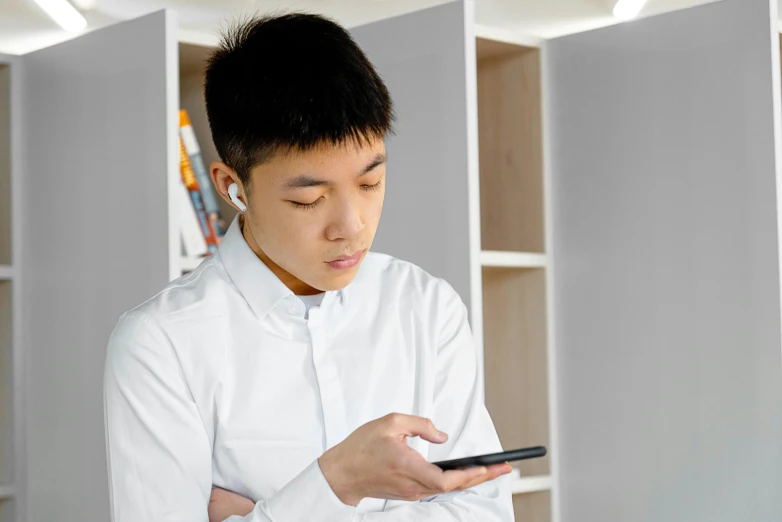 a man in a white shirt looking at a cell phone, inspired by Ye Xin, trending on pexels, avatar image, wearing modern headphone, hunched shoulders, male teenager