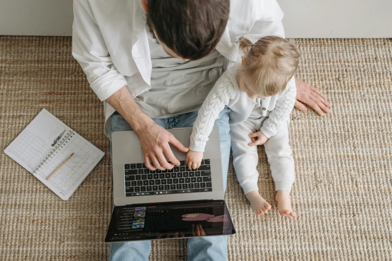 a man sitting on the floor with a baby using a laptop, pexels, computer art, top of pinterest, daughter, official screenshot, holding notebook