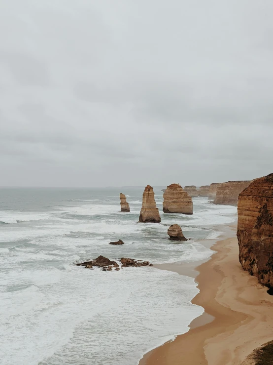 a sandy beach next to the ocean on a cloudy day, by Liza Donnelly, pexels contest winner, australian tonalism, majestic spires, wide high angle view, chiseled formations, view from the streets