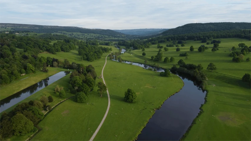 a river running through a lush green field, a picture, by John Atherton, drone camera lens orbs, brockholes, flowing hills, high quality screenshot