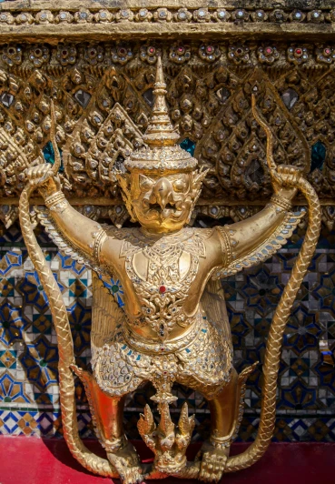 a gold statue sitting on top of a red table, a statue, ornate tiled architecture, closeup of arms, bangkok, standing astride a gate