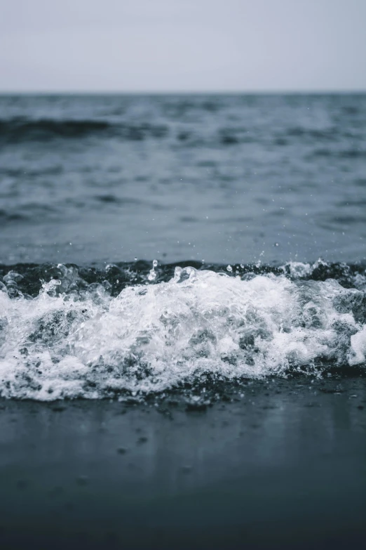 a black and white photo of a body of water, an album cover, unsplash, blue crashing waves, black sand, water droplets, blurred