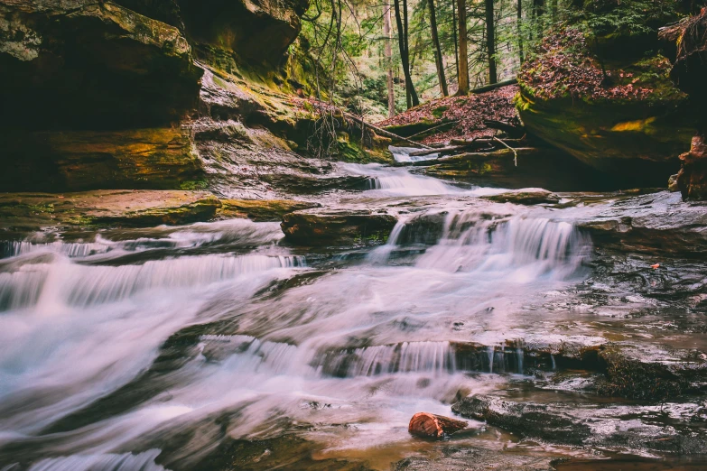 a stream running through a lush green forest, unsplash contest winner, wisconsin, sandstone, pink waterfalls, rocks falling